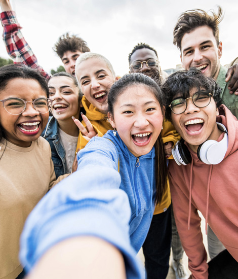 Multiracial friends taking big group selfie shot smiling at camera -Laughing young people standing outdoor and having fun – Cheerful students portrait outside school – Human resources concept